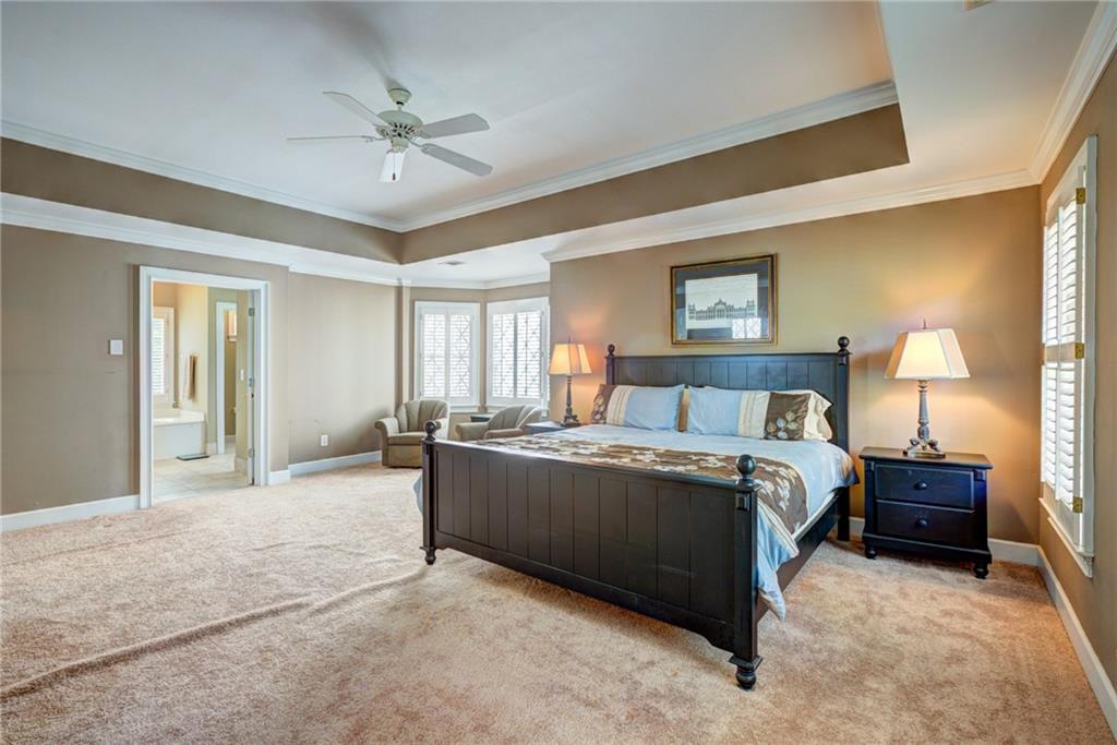 Bedroom with a dark wood bed, tray ceiling, and shuttered bay windows.