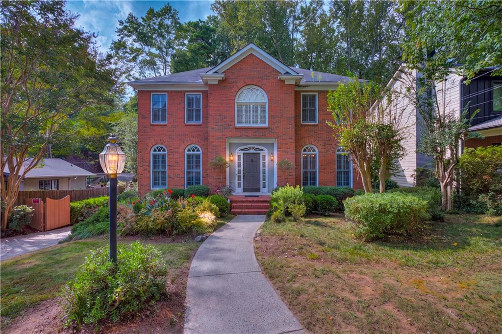 Two-story red-brick house with arched windows, a curved walkway, landscaped shrubs, and a garden lamp.