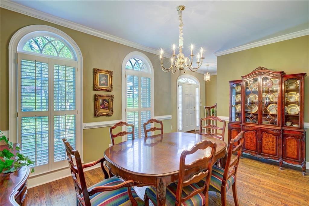 Dining room with an oval wooden table, chandelier, china cabinet, and tall arched windows.