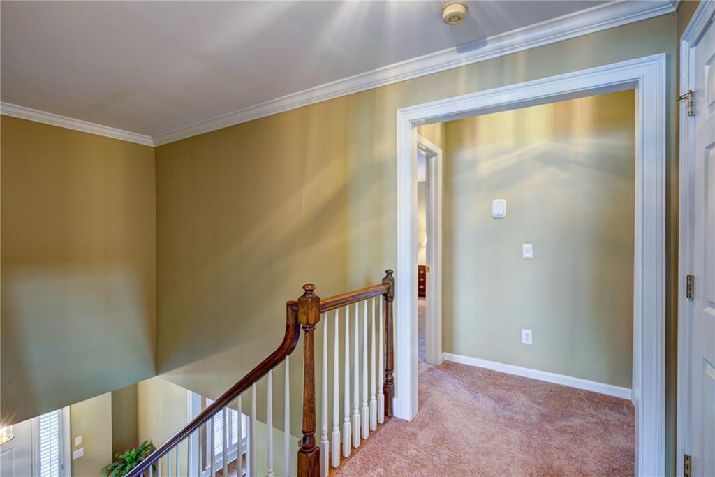 Upstairs hallway with a wood-and-white stair railing and sunlight across olive-green walls.