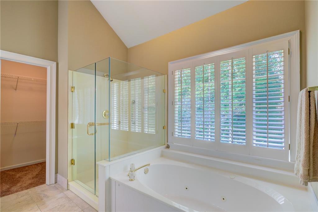 Bathroom with a built-in soaking tub, glass shower, and plantation shutters.