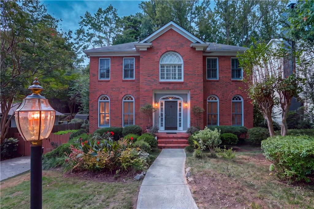 Two-story red brick house with an arched upper window, landscaped garden, and curved walkway.