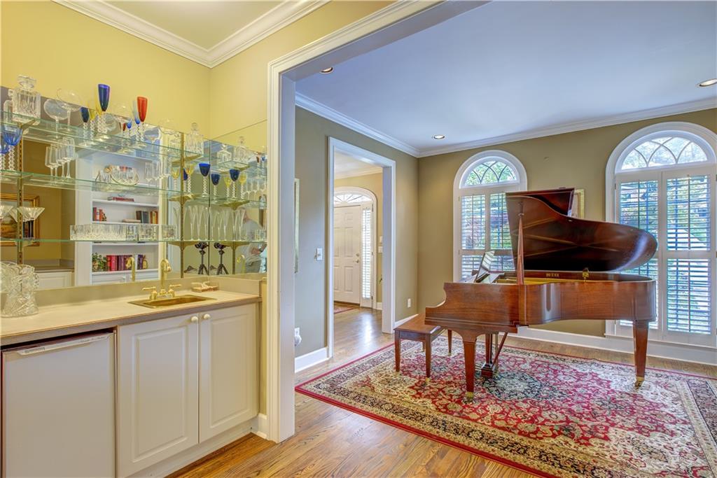 Music room with a grand piano, arched shuttered windows, and an adjoining wet bar.