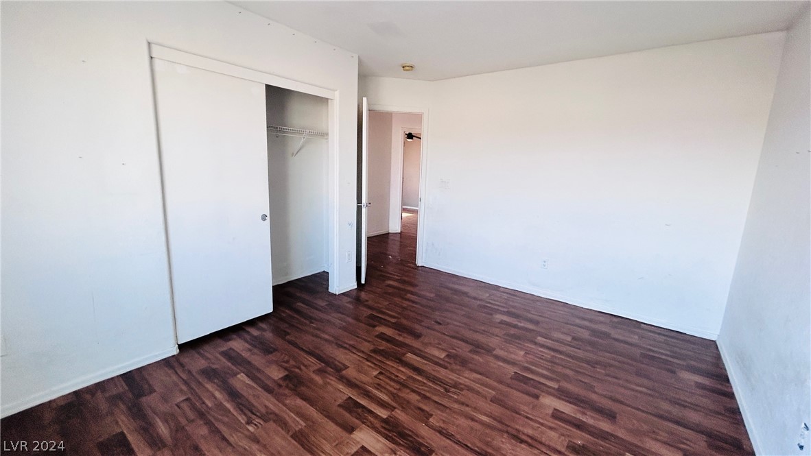 Empty bedroom with dark wood-look flooring and an open closet.