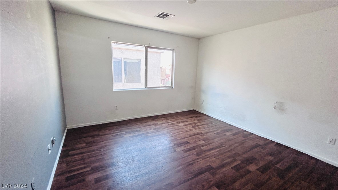 Empty bedroom with dark wood-look flooring, white walls, and a window.