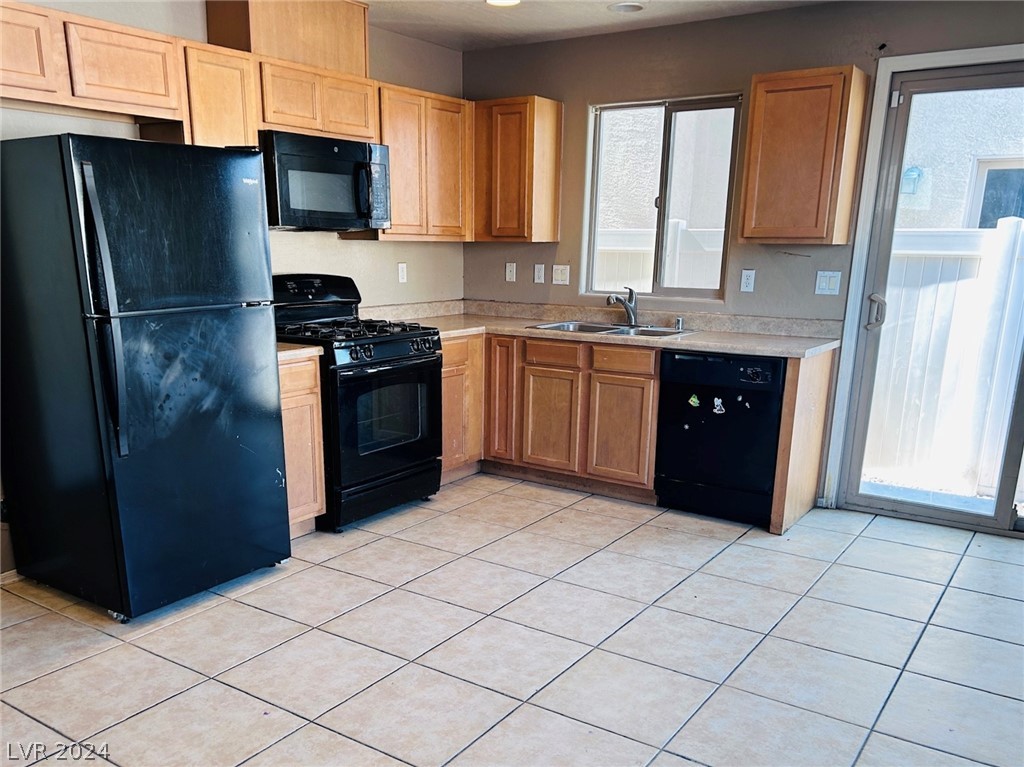 Kitchen with wood cabinets, black appliances, tiled floors, and a sliding glass patio door.