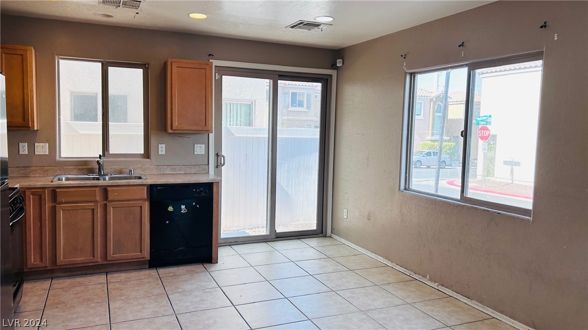 Unfurnished kitchen with brown cabinets, tiled floors, and a sliding glass door beside a large window.