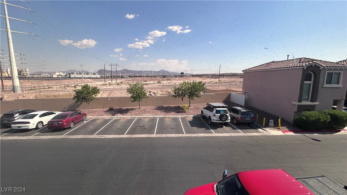 Parking area facing open desert land, utility lines, distant mountains, and a neighboring stucco building.
