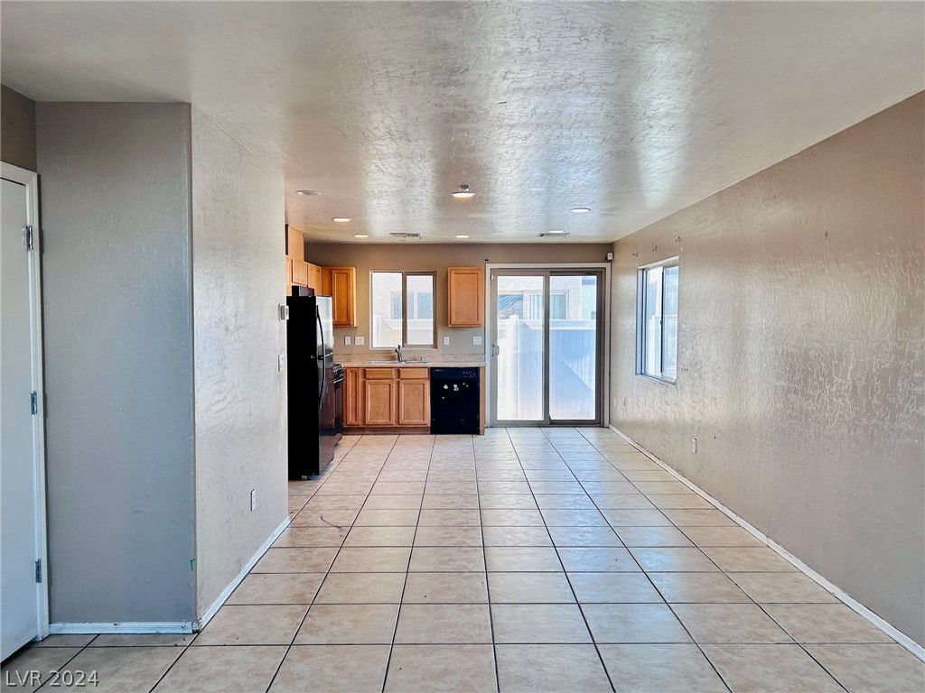 Unfurnished tiled living and dining area leading to a wood-cabinet kitchen and sliding glass door.