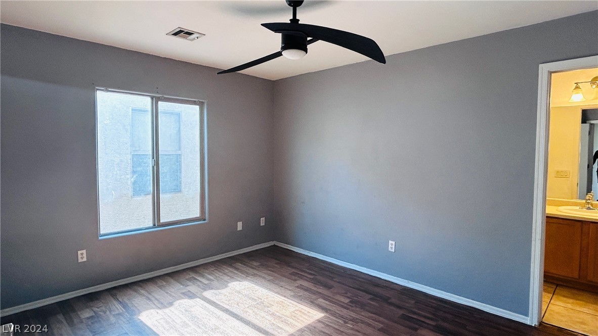 Vacant bedroom with gray walls, dark wood-look flooring, and a black ceiling fan beside a bathroom doorway.