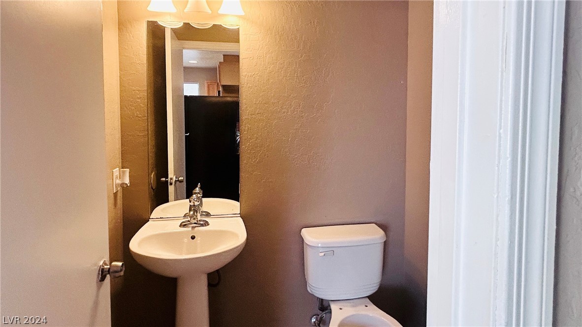 Bathroom with a white pedestal sink, mirror, and toilet against brown walls.