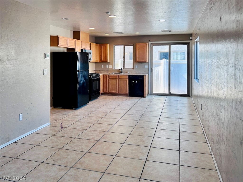 Kitchen with light wood cabinets, black appliances, tiled floor, and sliding glass doors to a fenced patio.