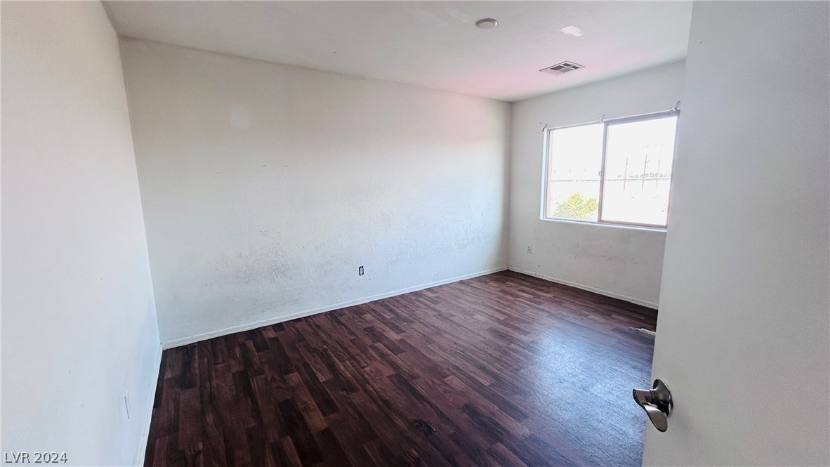 Vacant room with dark wood-look flooring, white walls, and a sunlit window.