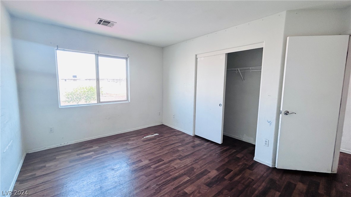 Vacant bedroom with dark wood-look flooring, a large window, and an open closet.