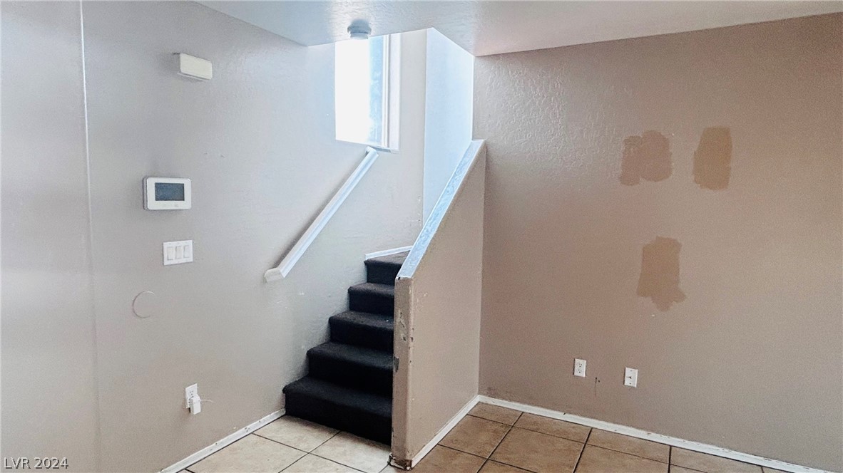 Vacant entryway with tiled floor, carpeted stairs, and patched walls.