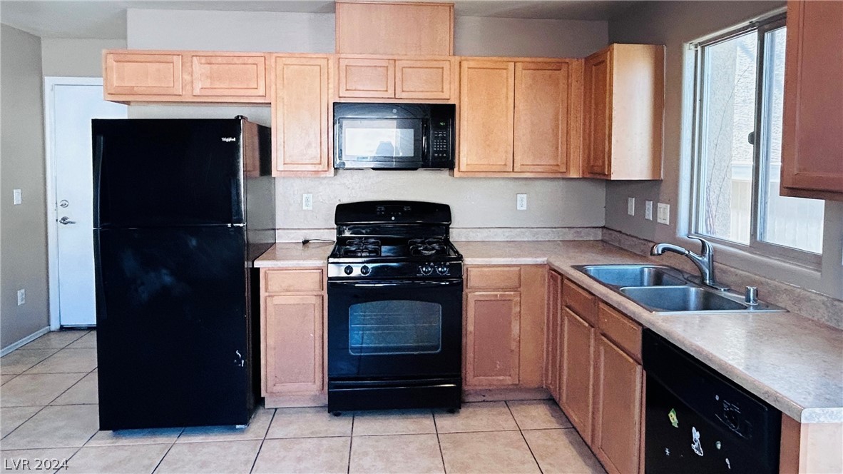 Kitchen with light wood cabinets, black appliances, and a double sink beneath a window.