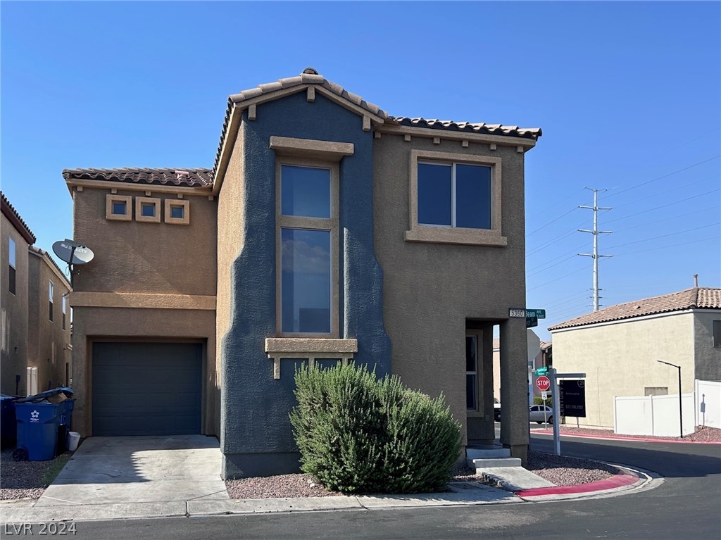 Two-story stucco home with a dark blue central facade, attached garage, and large shrub by the entry.