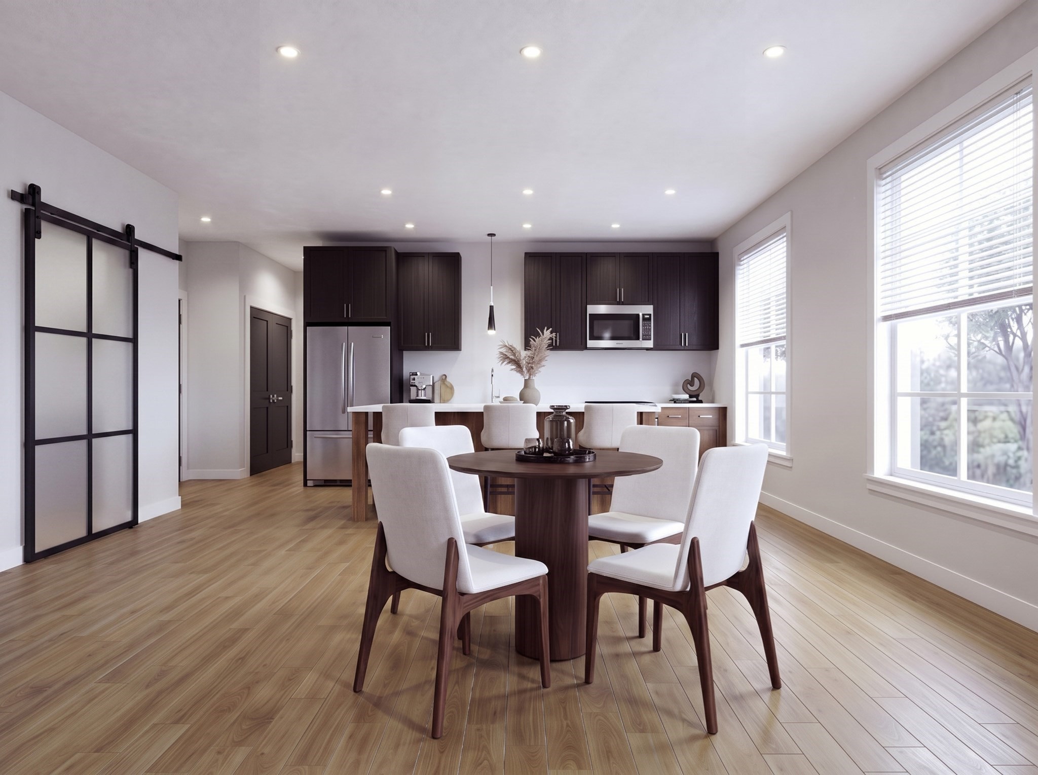 Open-plan kitchen and dining area with dark cabinets, a round table, and large bright windows.