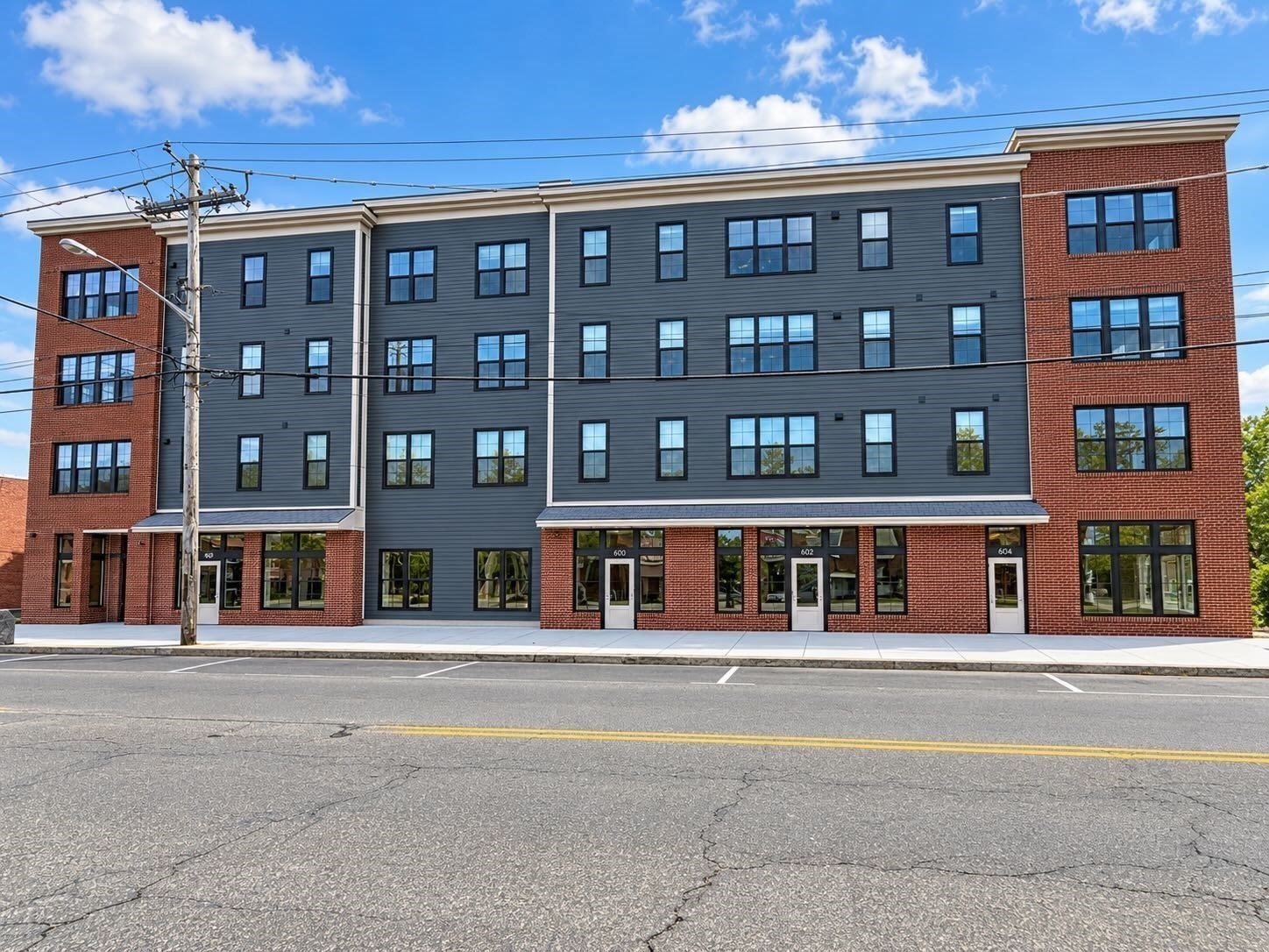 Four-story multifamily building with gray siding, red-brick sections, and street-facing entrances.
