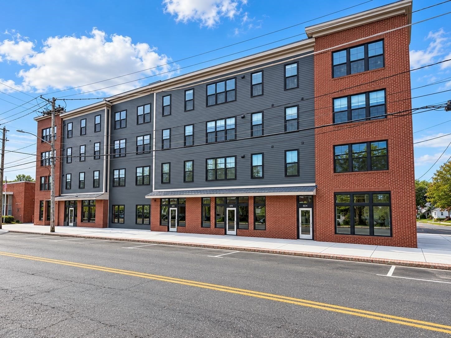 Multi-story apartment building with gray siding, red brick ends, and rows of black-framed windows.