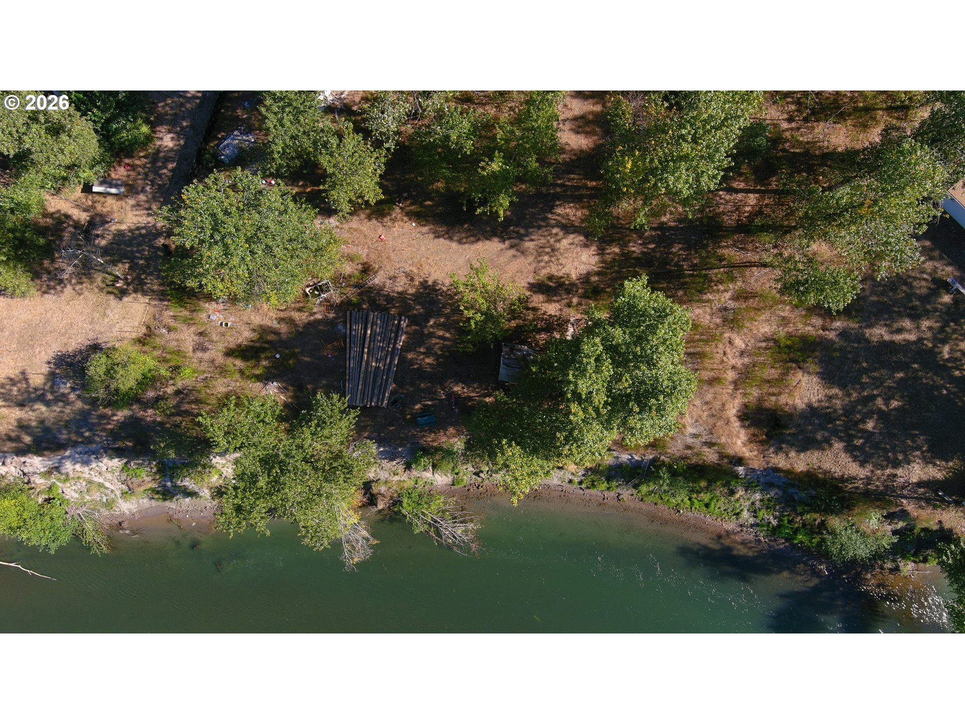 Aerial view of a wooded riverfront property with a broad clearing along the shoreline.