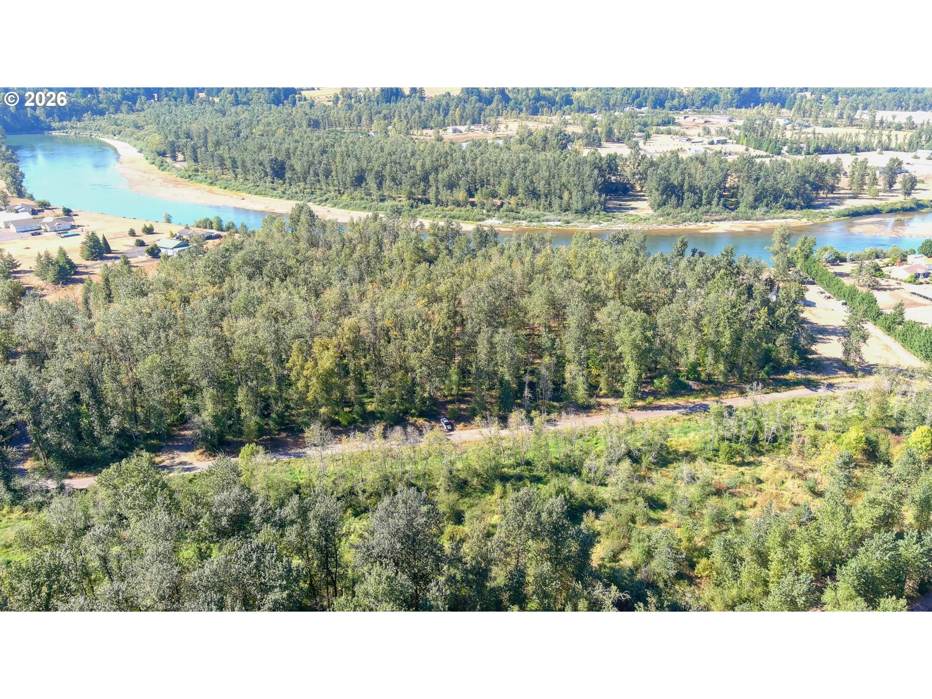 Aerial view of dense woodland beside a winding river and nearby homes.