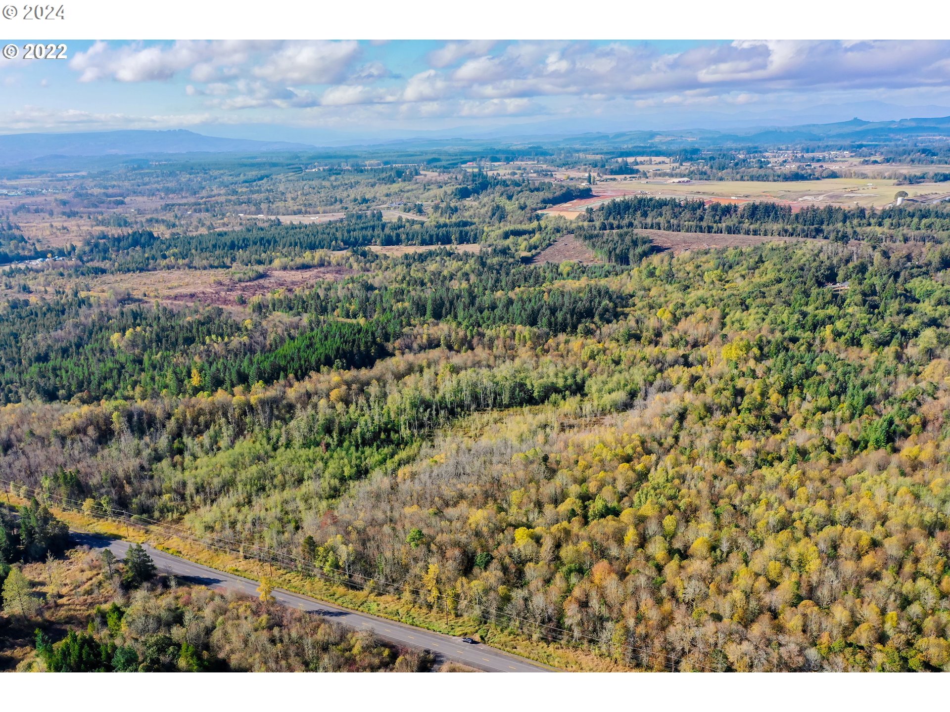 Aerial view of wooded land, a road, and distant mountain ridges.