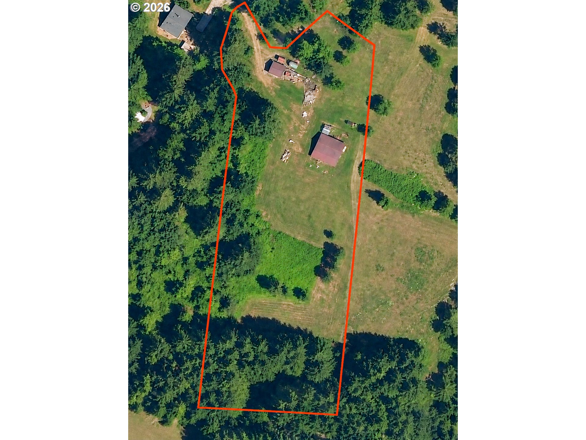 Aerial view of a wooded parcel outlined in red, with cleared land and several buildings.