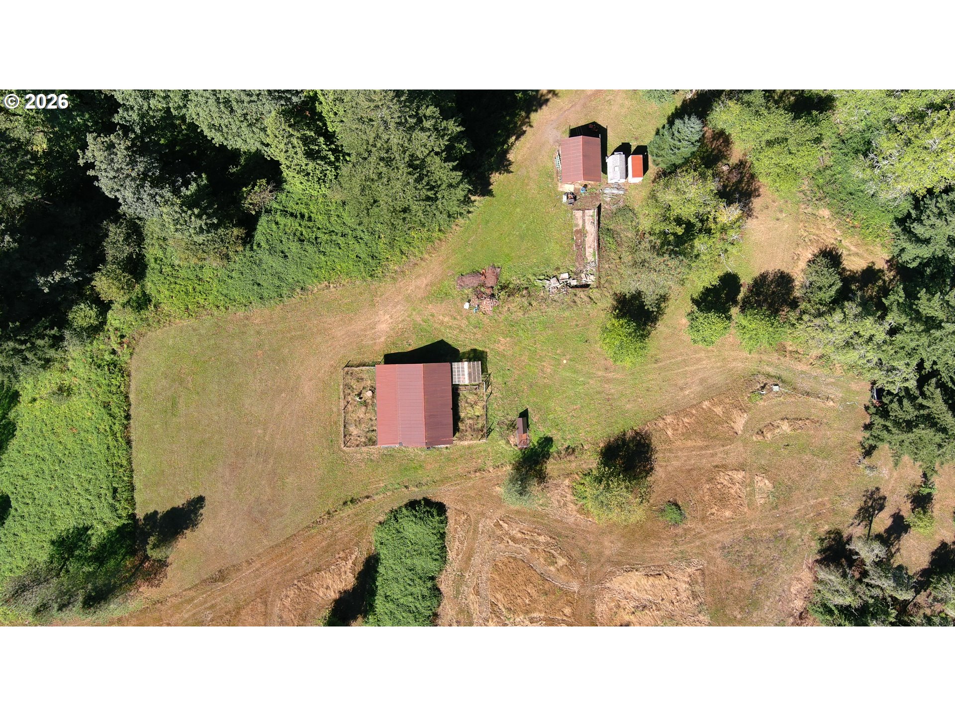 Aerial view of a wooded property with cleared grounds, dirt tracks, and several outbuildings.