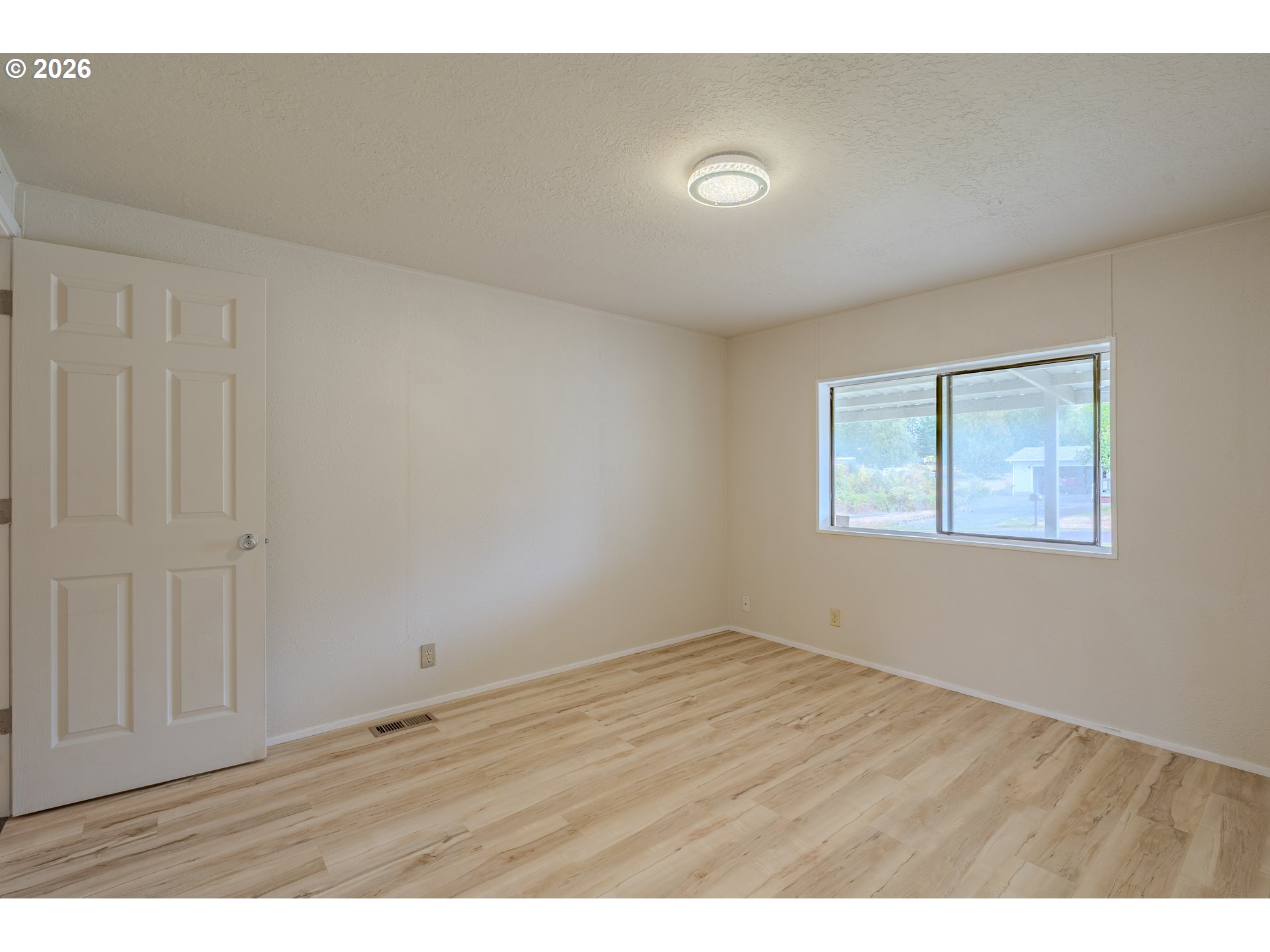 Empty room with light wood-look flooring, cream walls, and a wide window.