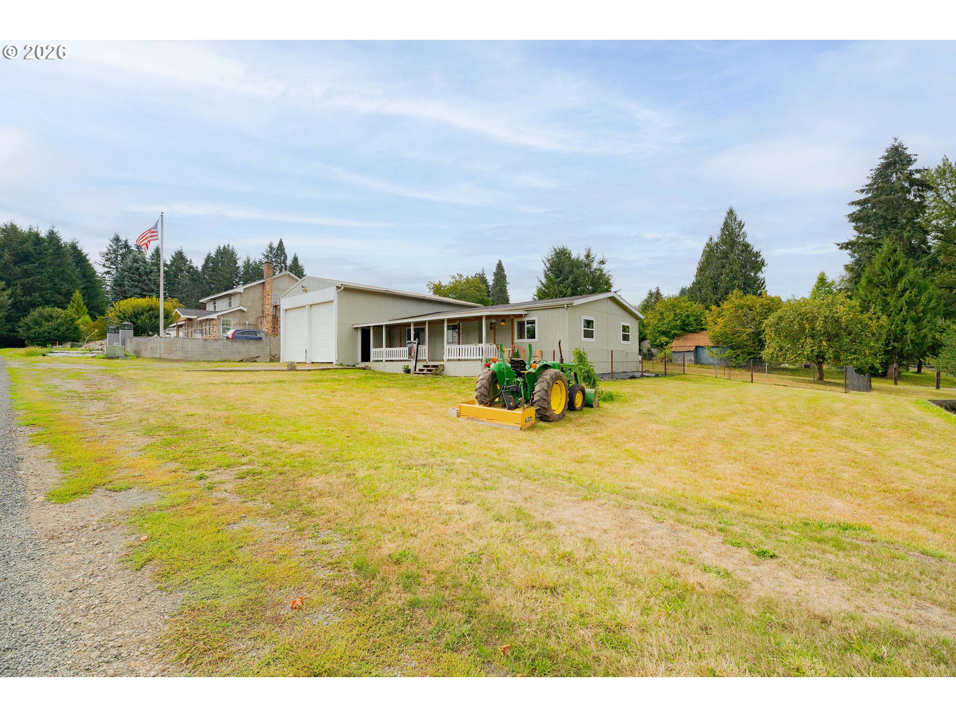 Home with attached garage and covered porch, green tractor parked on the grassy yard.
