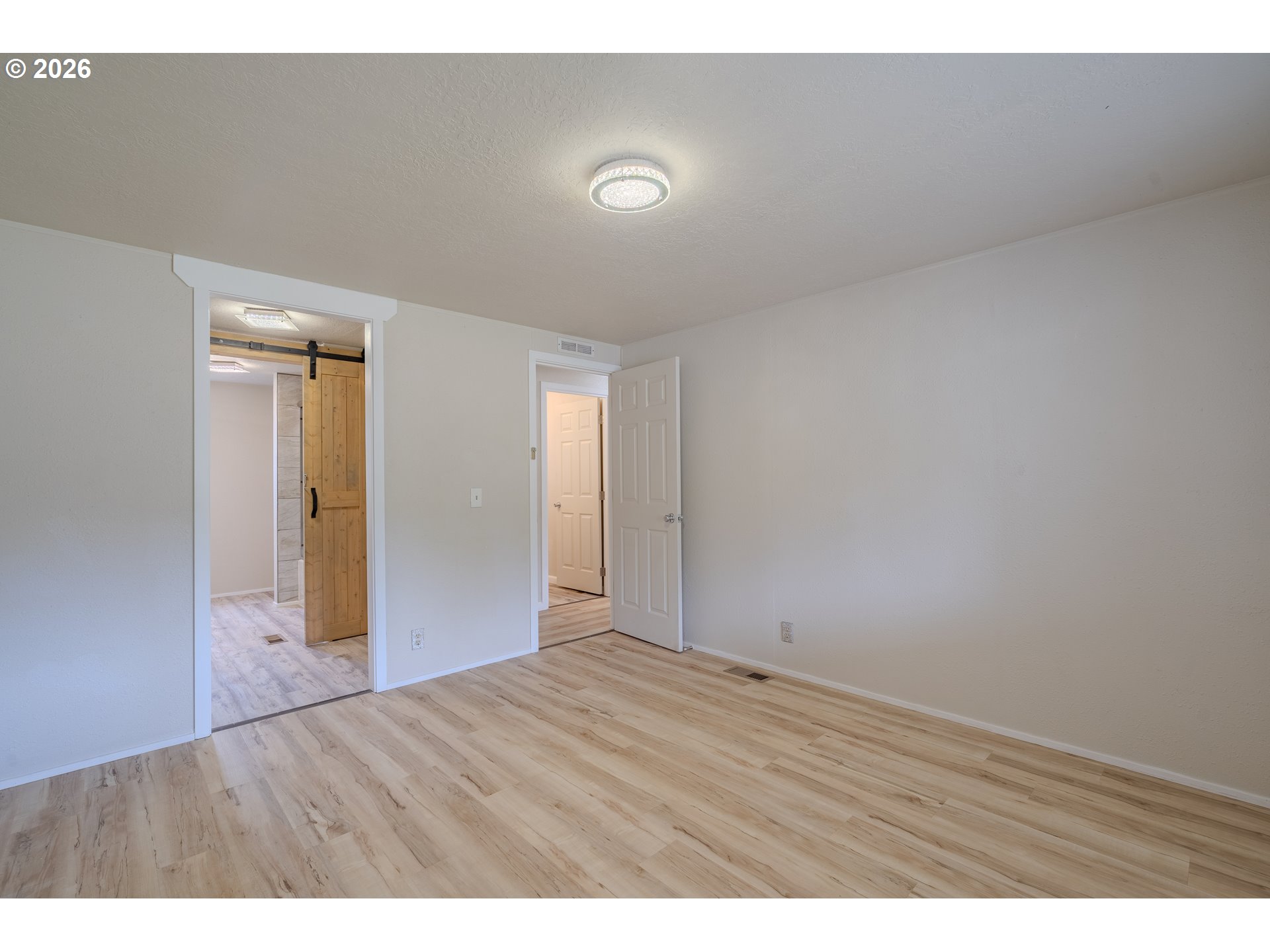 Empty room with light wood-look floors, a sliding barn door, and an open doorway to the hall.