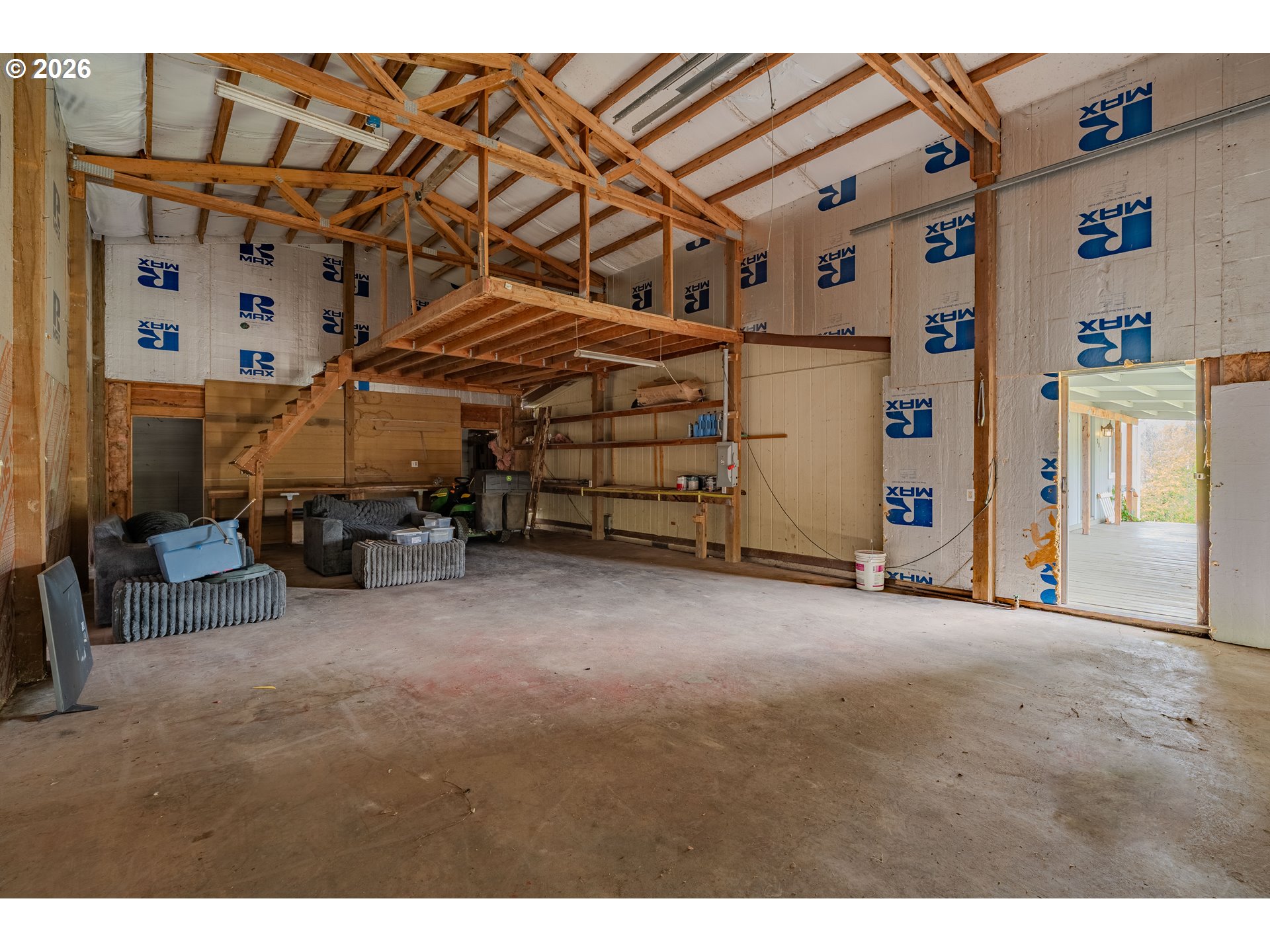 Unfinished garage with exposed timber framing, a raised loft, and an open exterior doorway.