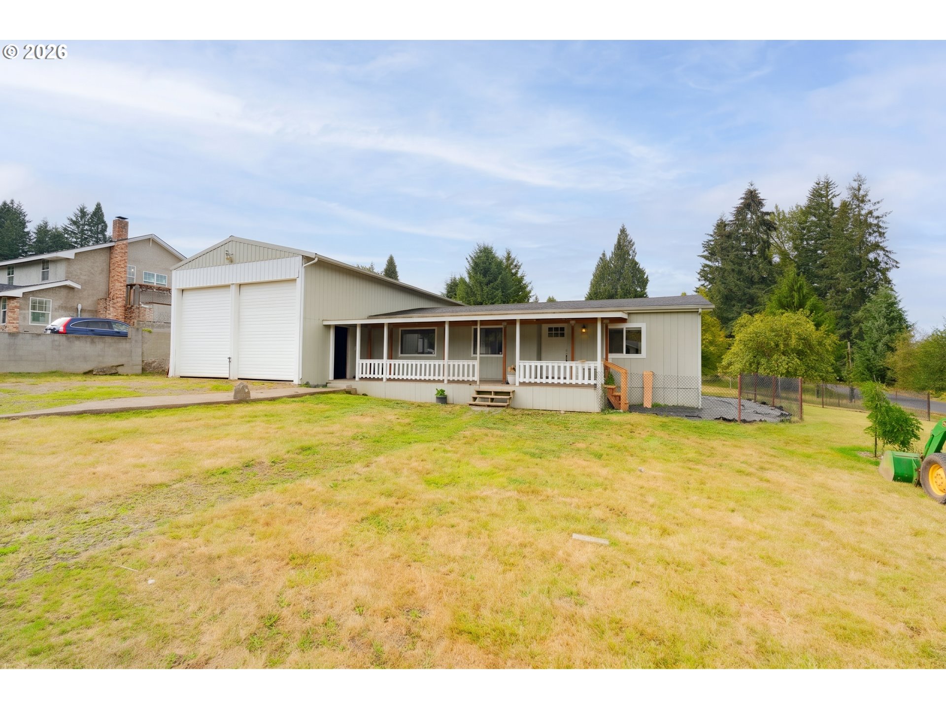 Single-story home with a covered porch, large garage, and broad dry lawn.