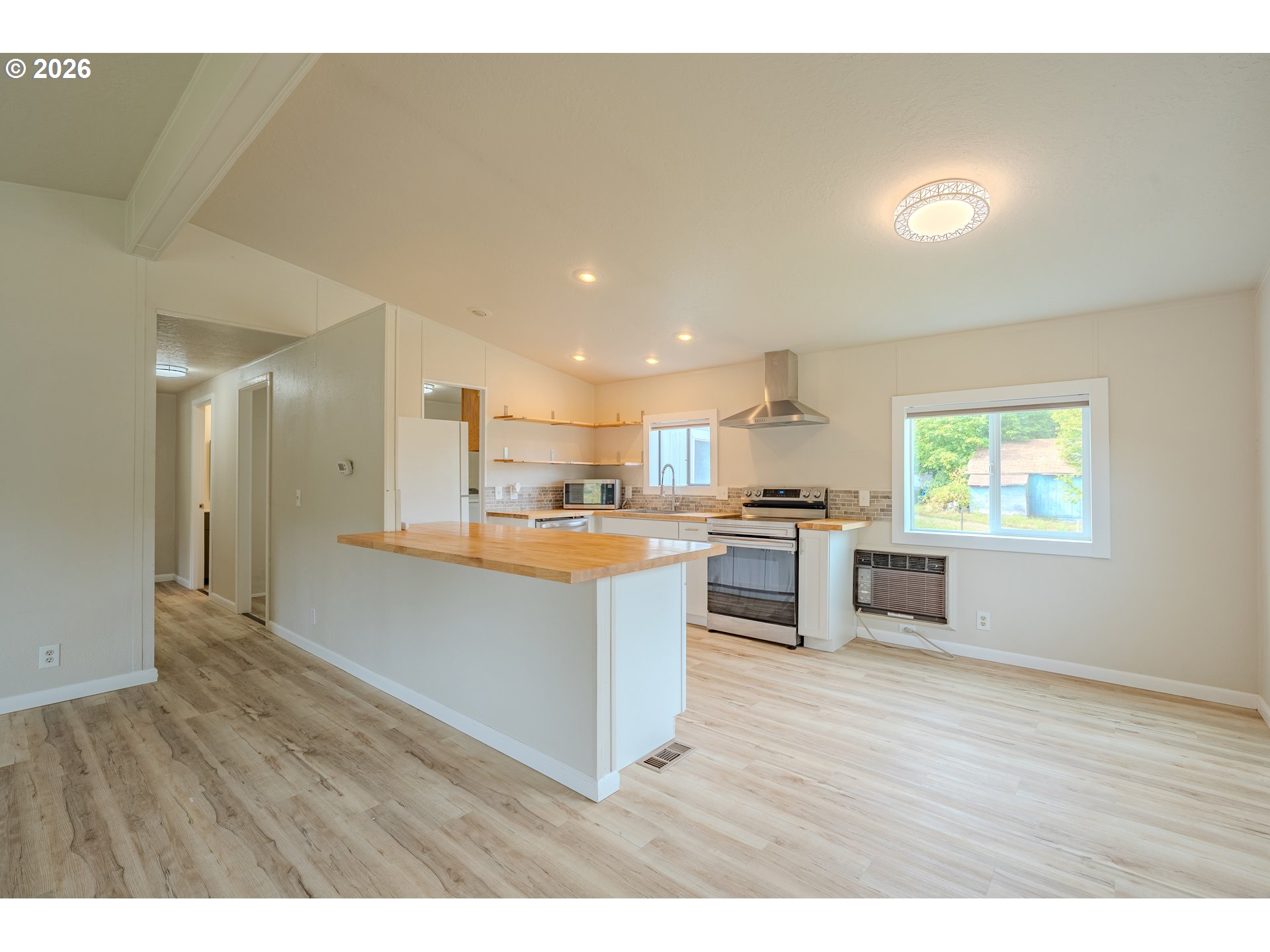 Unfurnished kitchen with a wood-topped peninsula, stainless steel range, open shelving, and light wood-look floors.