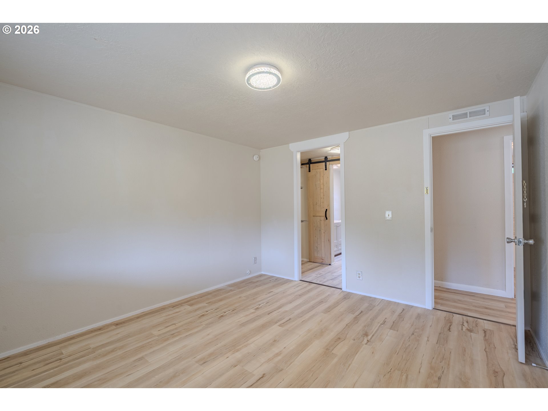 Vacant room with wood-look flooring and a doorway to an adjoining space with a wooden sliding barn door.