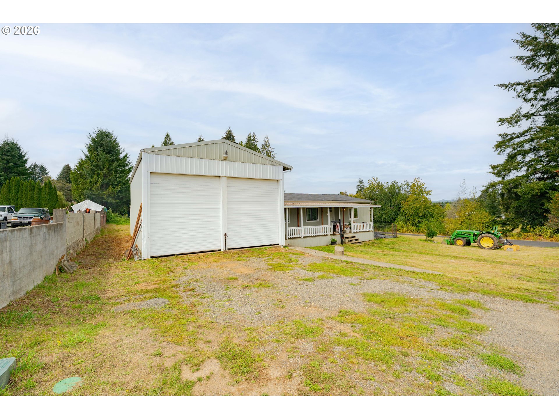 House and large detached garage with twin doors, covered porch, gravel yard, and green tractor.