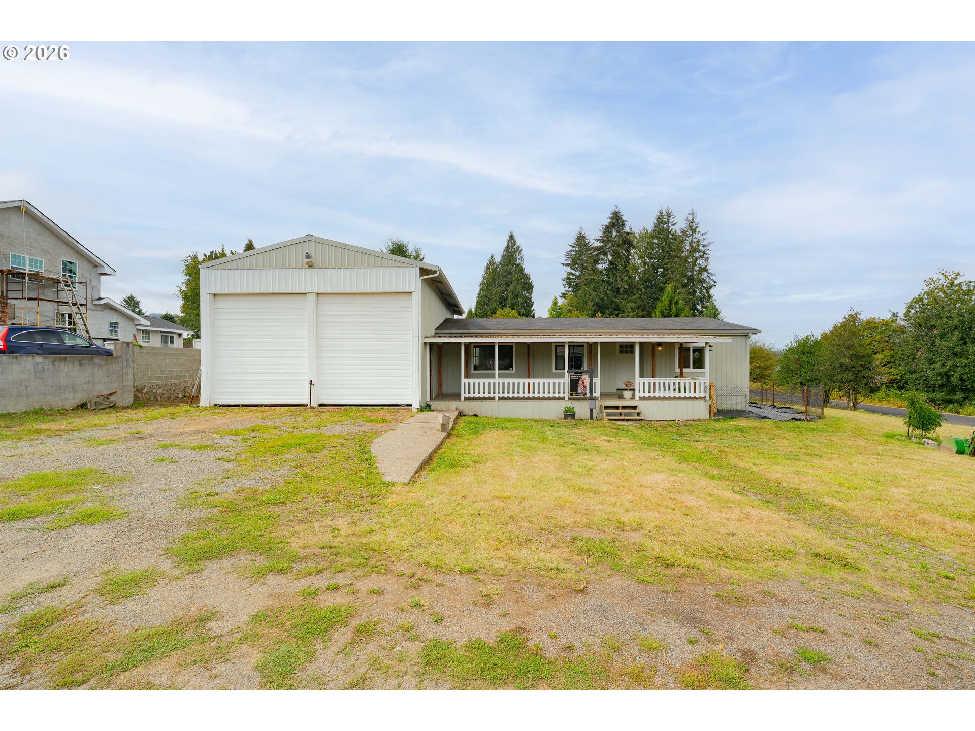 Single-story home with a covered porch and oversized two-door garage beside a gravel driveway.