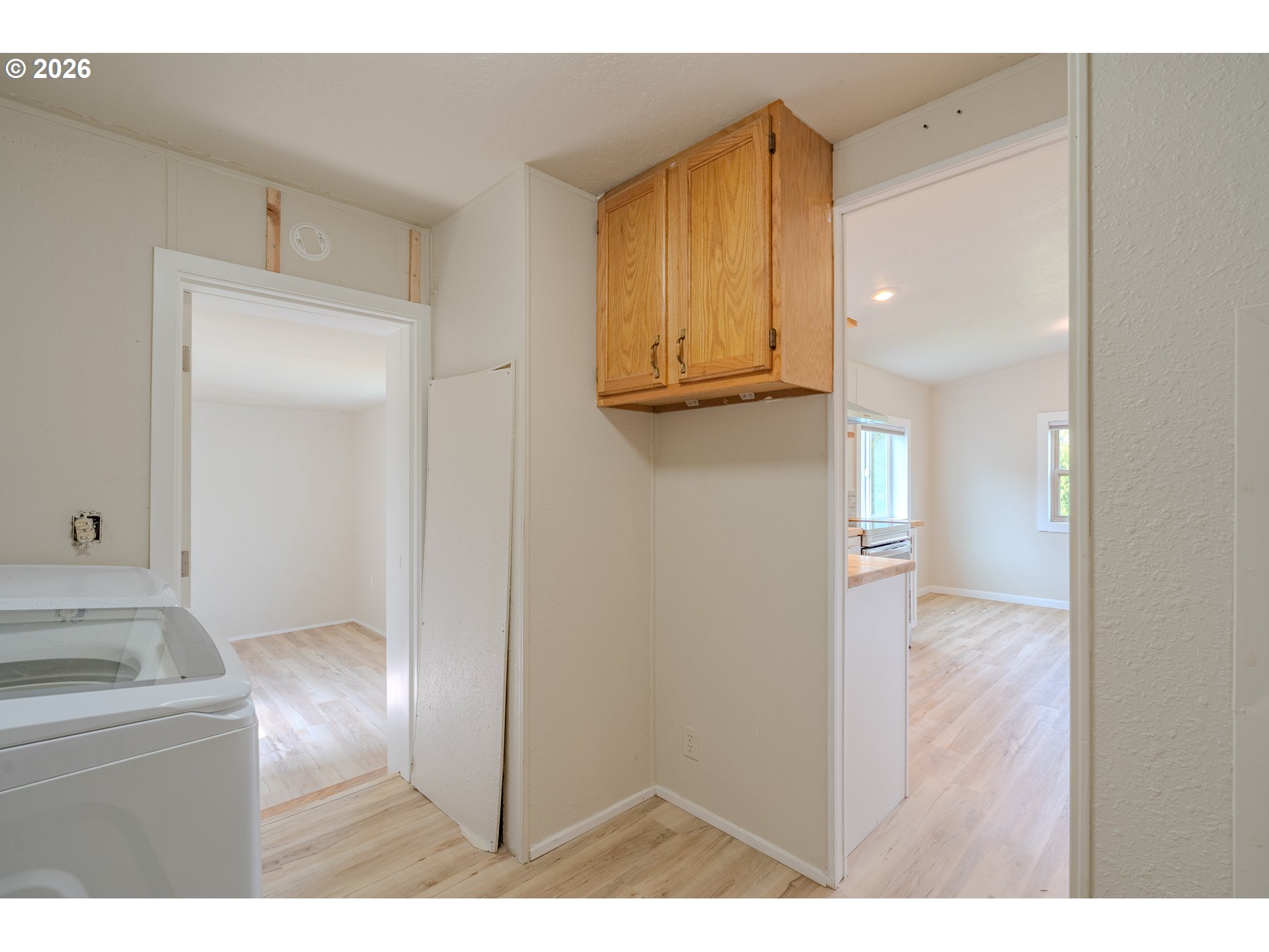 Laundry room with a washing machine, wooden wall cabinet, and doorways to bright adjoining rooms.