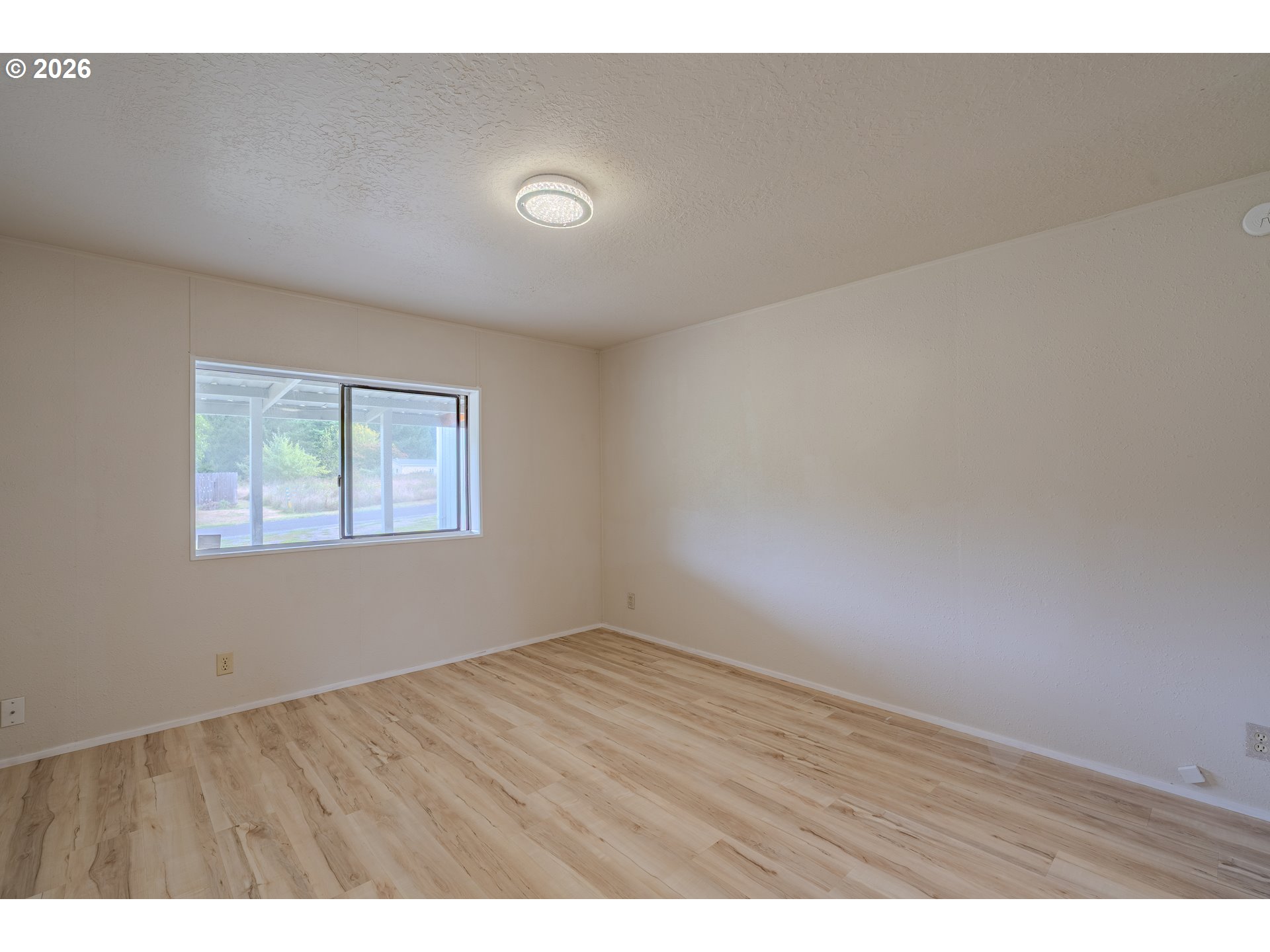 Empty room with light wood-look flooring, beige walls, and a wide sliding window.