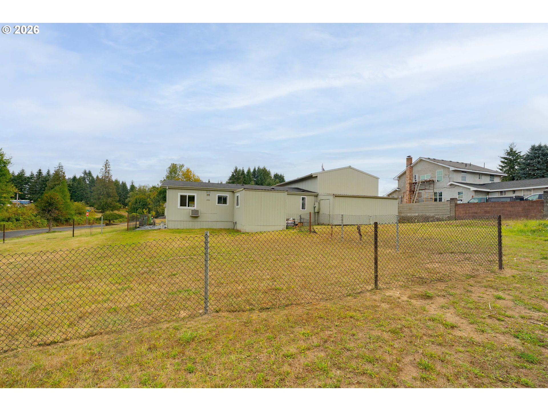 Pale green building behind a chain-link fence enclosing a grassy yard.