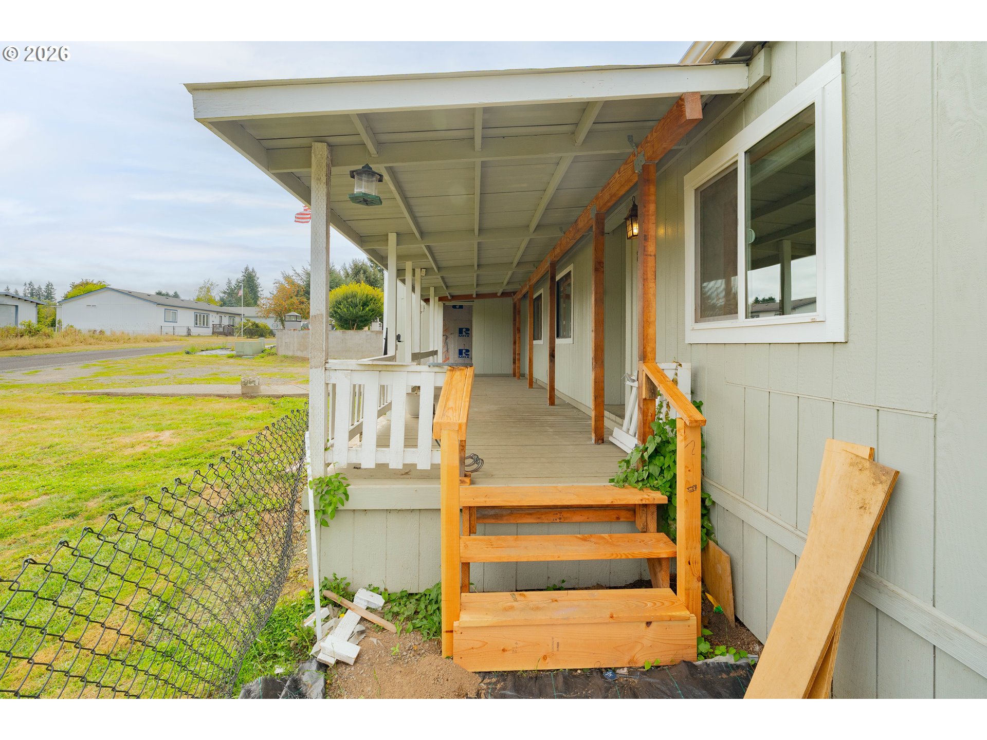 Covered house porch with new wooden steps and railings beside a fenced yard.