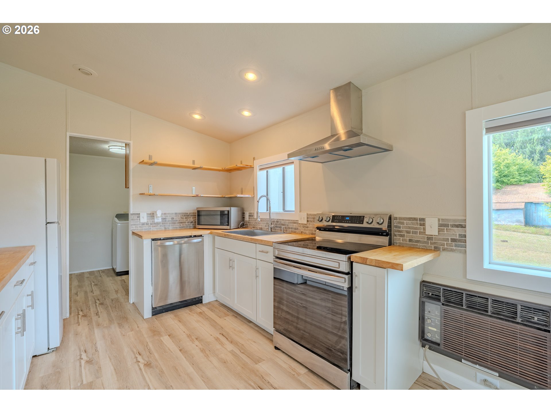 Kitchen with white cabinets, wood counters, stainless appliances, open shelves, and a window air conditioner.