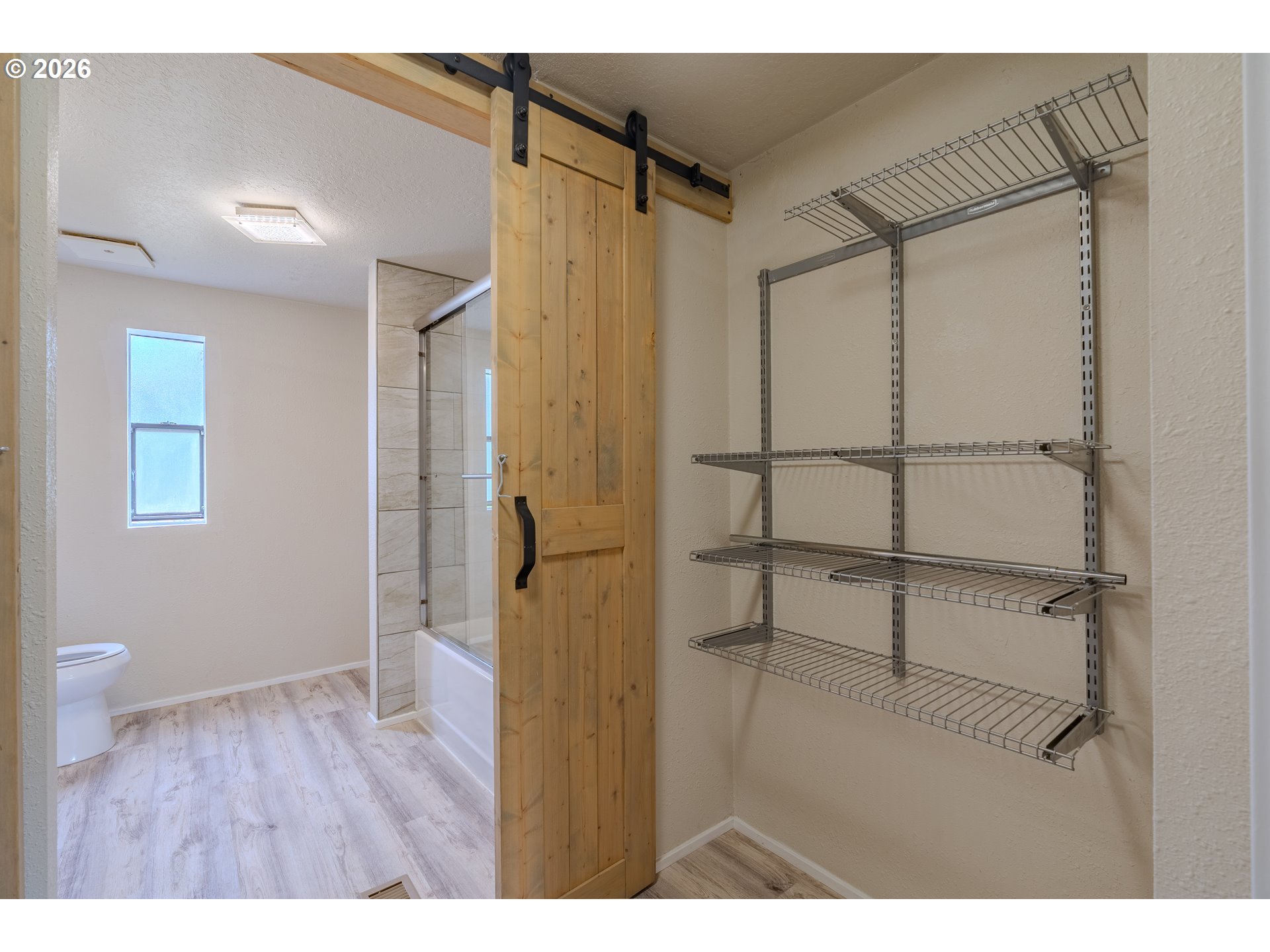 Walk-in closet with empty wire shelves beside a bathroom, separated by a wood sliding barn door.