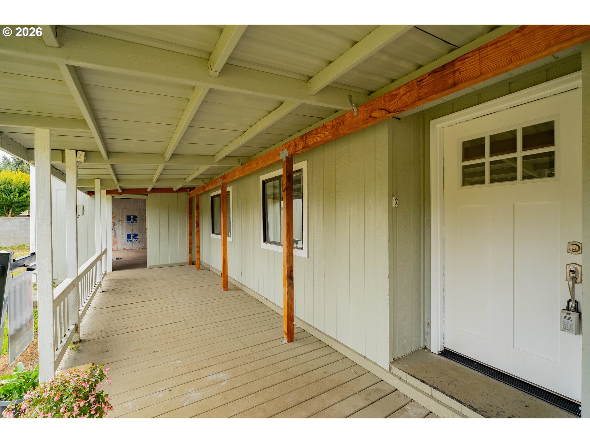 Covered porch with exposed wood posts and beam, plank flooring, and a white entry door.
