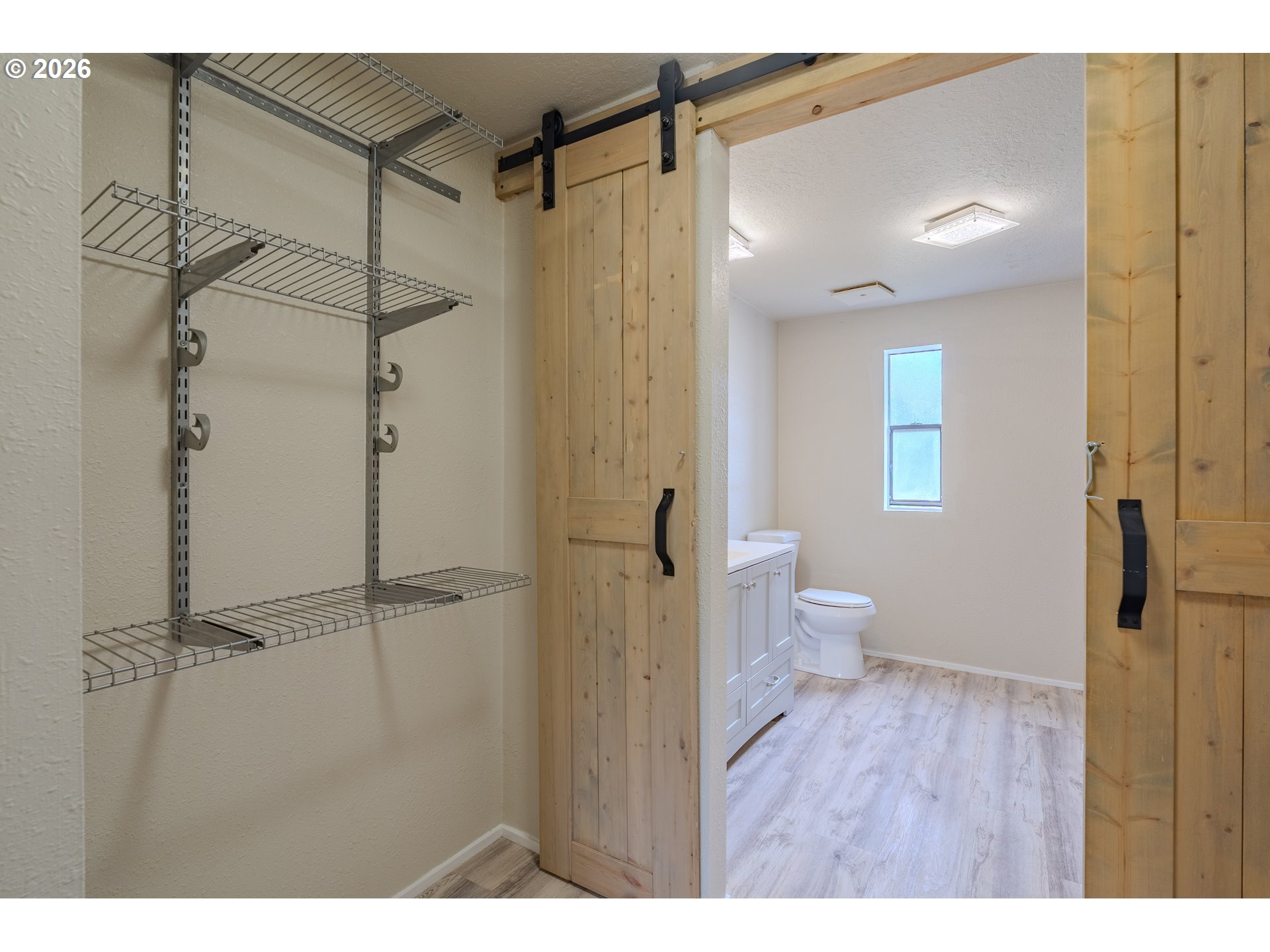 Bathroom and walk-in closet with wire shelving, sliding barn door, white vanity, and toilet.