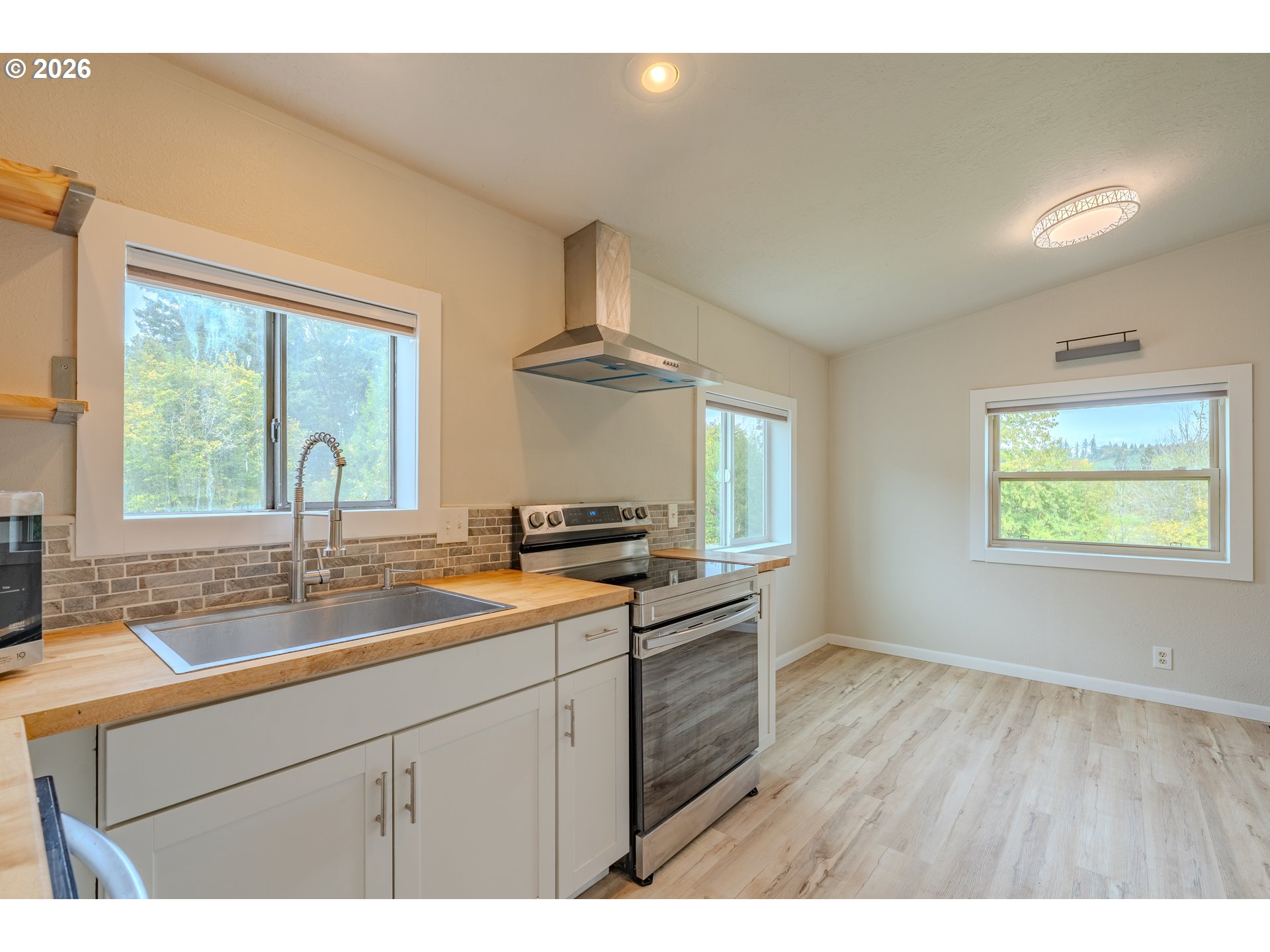 Vacant kitchen with butcher-block counters, stainless steel range, tiled backsplash, and large windows.