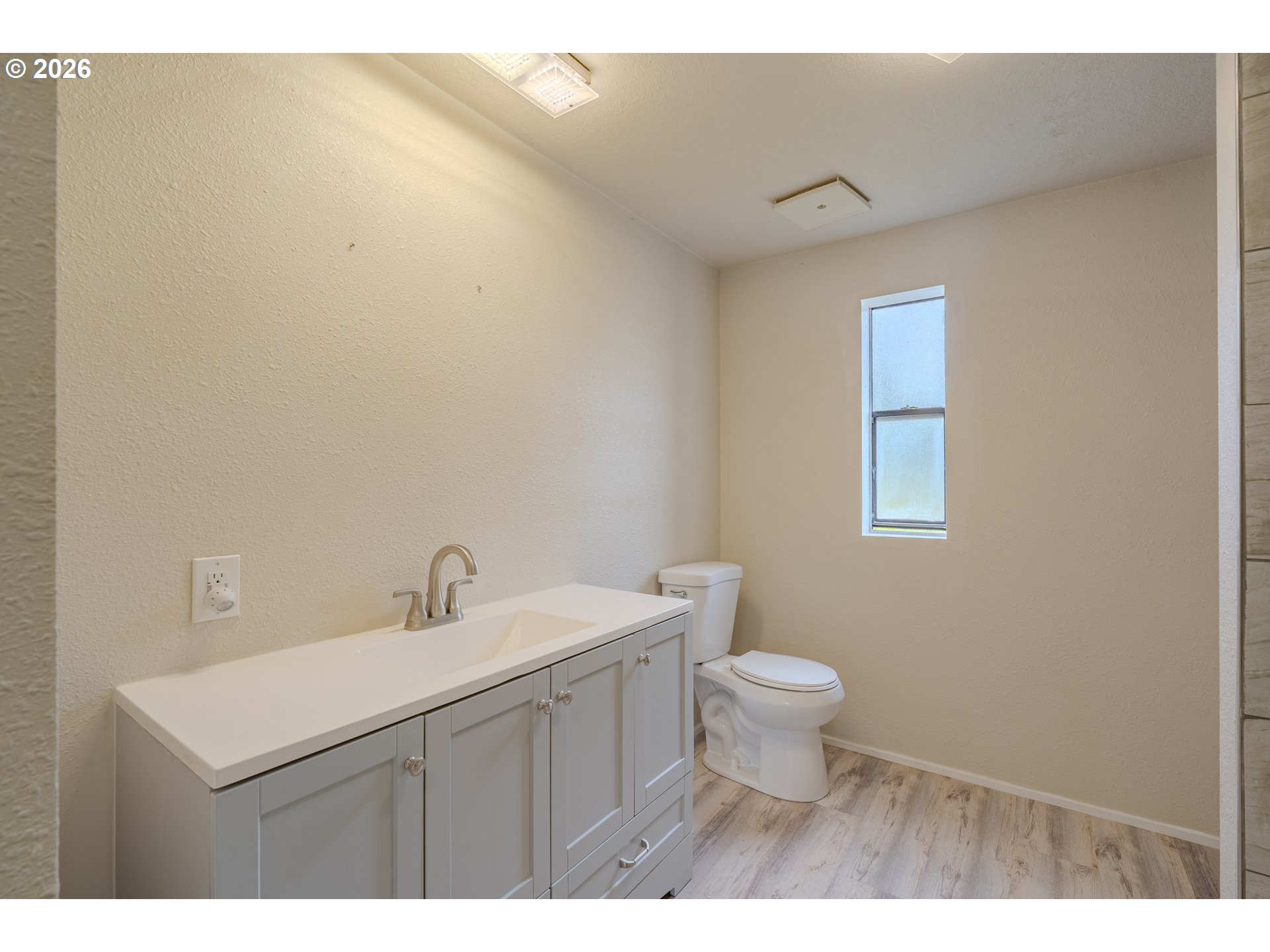 Bathroom with a gray vanity, white countertop, toilet, and narrow window.
