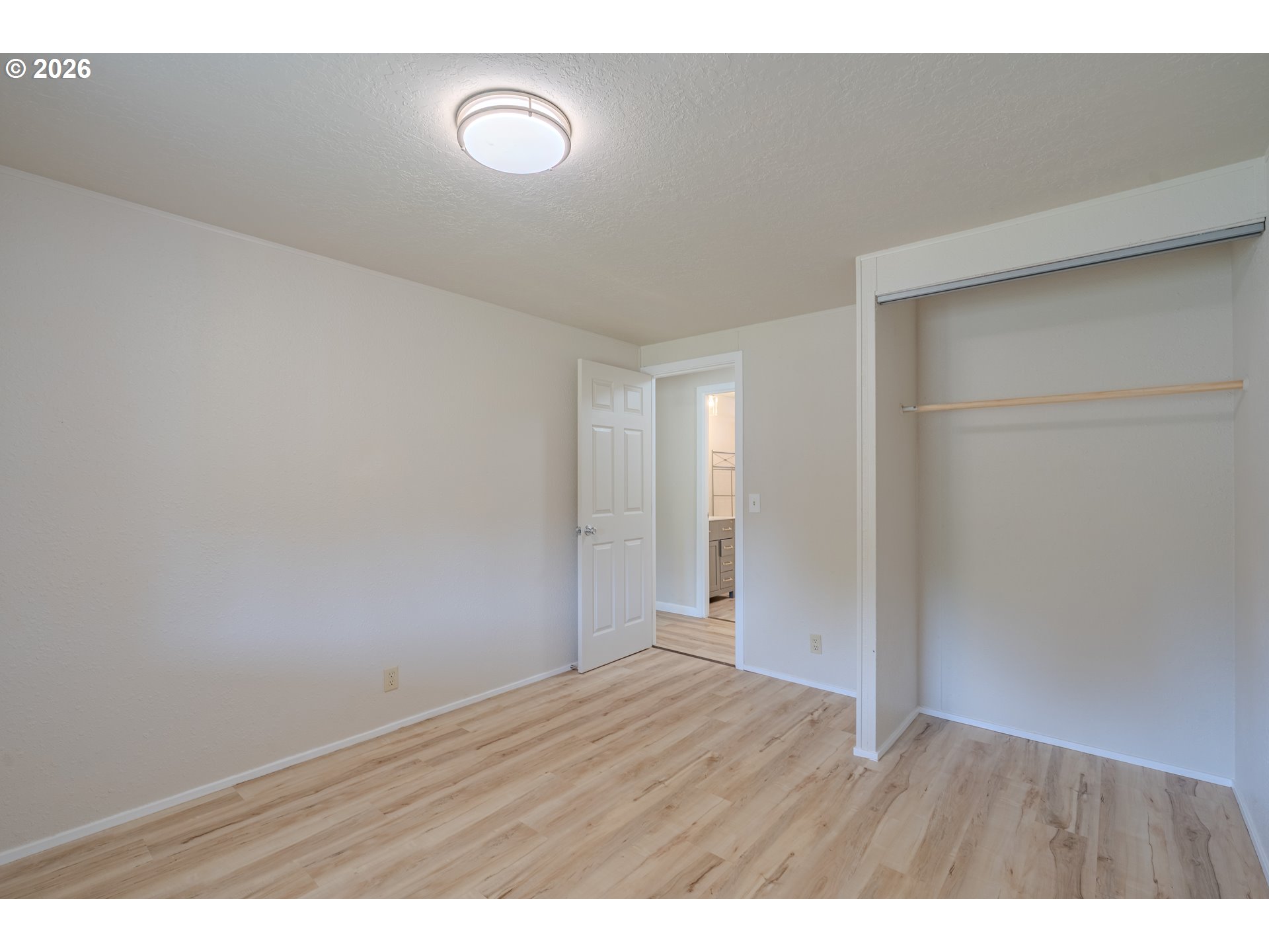 Empty bedroom with light wood flooring and an open closet beside the doorway.