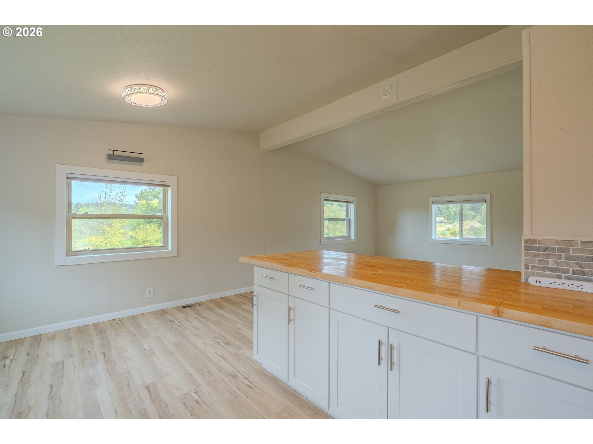 Empty kitchen with white cabinets, a long wood countertop, and three windows.